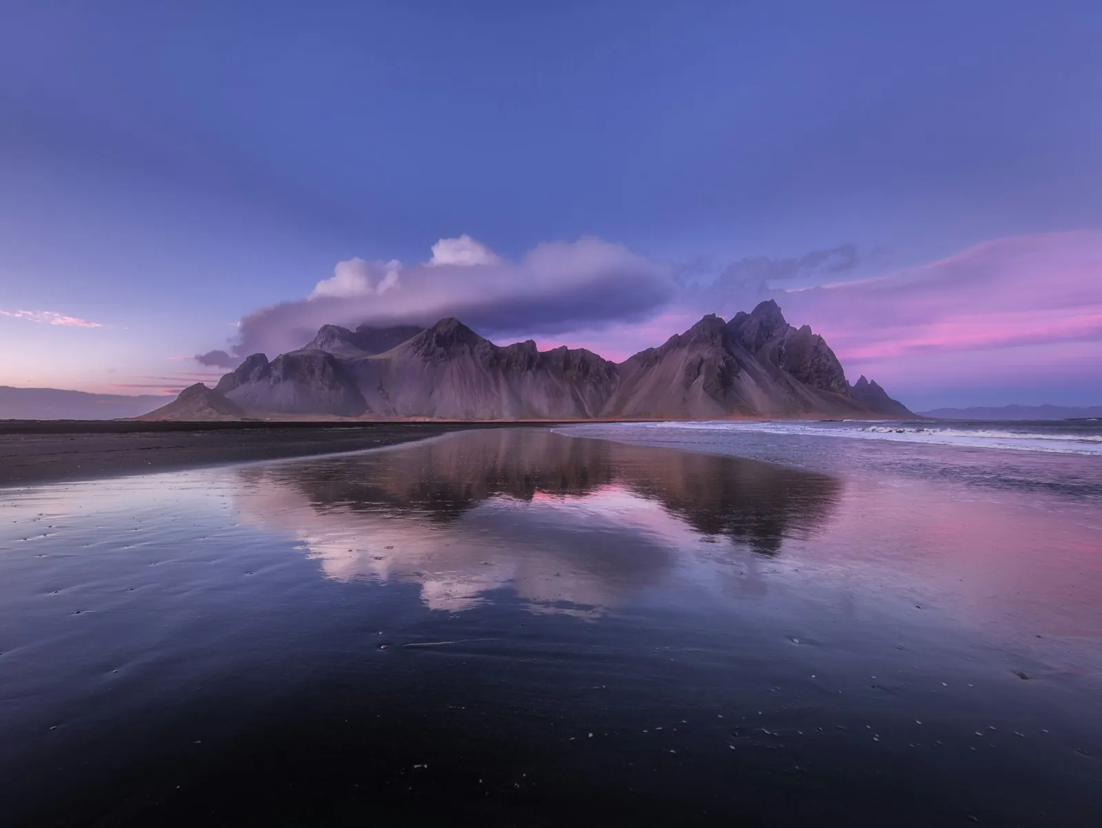 Vestrahorn mountain mirrored in wet black volcanic sand under a violet Icelandic sky.