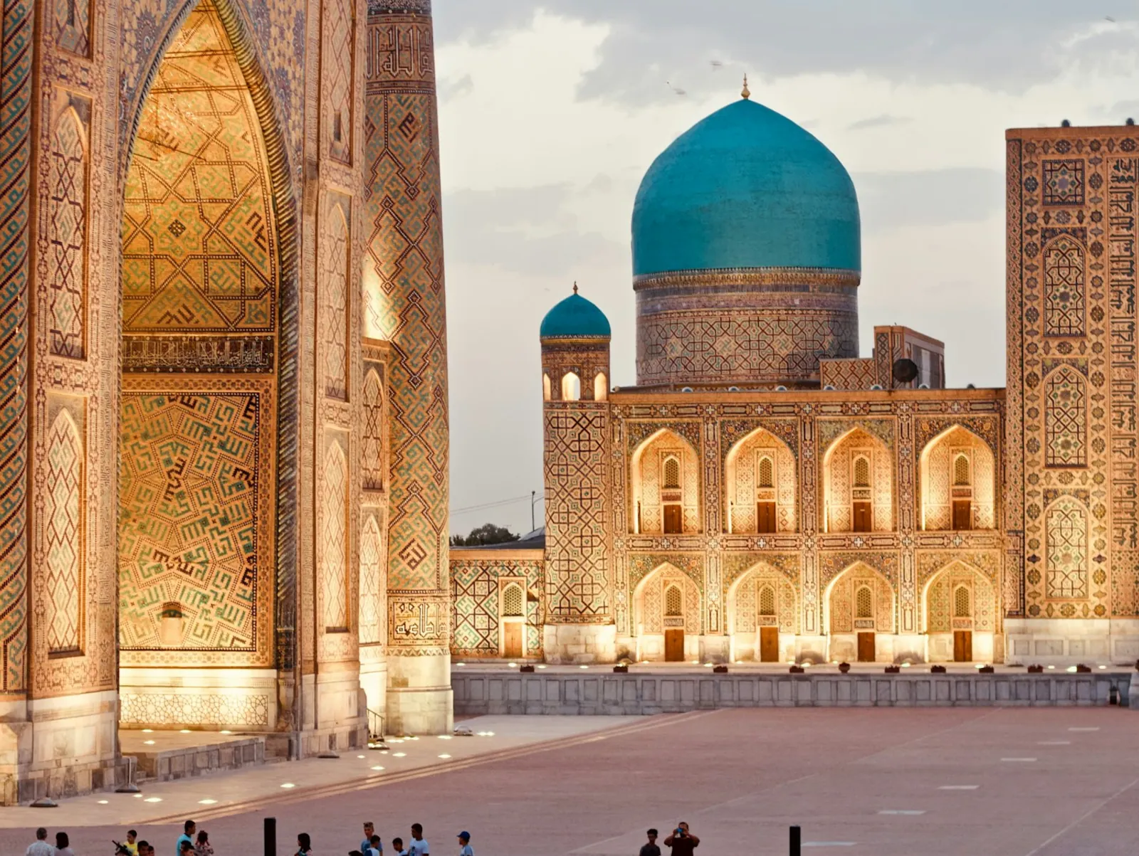 The Tilya-Kori madrasah on Samarkand's Registan square, its turquoise dome and tiled facade lit gold in the late afternoon.